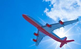 avión de pasajeros rayas rojas blancas volando en el cielo en un día azul brillante, nubes blancas durante el día. la vista mira hacia arriba debajo del avión. representación 3d foto