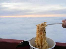 Instant noodles in a cup And white forks Background image of the sea fog in the morning before sunrise. photo