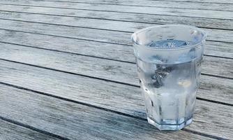 agua clara o soda en un vaso transparente para cerveza. agua fría en un vaso con cubitos de hielo, burbujas en el vaso. colocado en un piso de tablones hay una luz que brilla en el vidrio. representación 3d foto