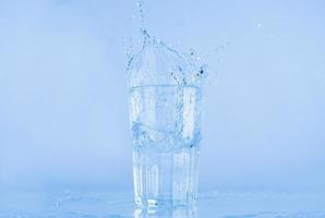 A glass of water splashed up. The water rose from a clear glass with a square. photo