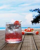 el néctar de fresas sin alcohol con soda no mezcla alcohol. las fresas frescas en una taza de cerámica están en el desenfoque de fondo colocadas en una mesa de madera. el restaurante en la playa y el mar. foto