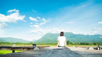 girl wearing a casual t-shirt Sit on a wooden walkway, see nature, mountains, rice fields, fresh air. and the morning sun bright blue sky white clouds photo