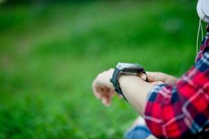 The girl watches the watch in hand, watches the time in a black watch, wears a red shirt and a green background. And there is a copy space. photo