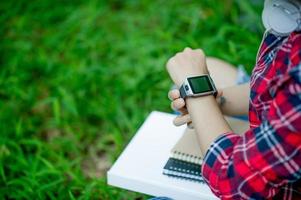 The girl watches the watch in hand, watches the time in a black watch, wears a red shirt and a green background. And there is a copy space. photo