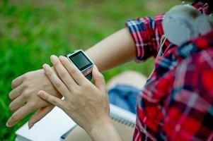 The girl watches the watch in hand, watches the time in a black watch, wears a red shirt and a green background. And there is a copy space. photo