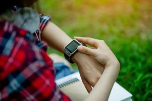 The girl watches the watch in hand, watches the time in a black watch, wears a red shirt and a green background. And there is a copy space. photo