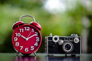 el reloj rojo y la cámara ponen sobre la mesa el tiempo y los conceptos de equipo de tiro de puntualidad y fotografía foto