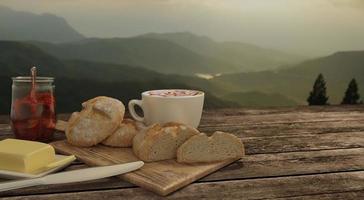 home made bread and  butcher in breakfast  concept on wooden table. Blur latte art coffee with chocolate sauce and caramel sauce  on Milk foam in white cup.   Background mountian view and sunrise photo