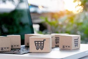 compras en línea: cajas de papel o paquetes con el logotipo de un carrito de compras en un teclado portátil. servicio de compra en la web online y ofrece servicio a domicilio. foto