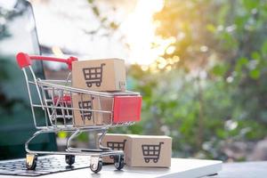 compras en línea: paquetes o cajas de papel con el logotipo de un carro de la compra en un carrito en un teclado portátil. servicio de compras en la web en línea. ofrece entrega a domicilio. foto