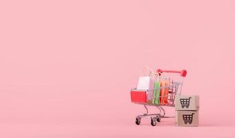 Shopping concept. Cartons or Paper boxes and shopping bag in red shopping cart on pink background. online shopping consumers can shop from home and delivery service. with copy space photo