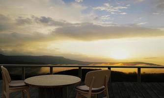 mesas y sillas de madera para relajarse en el balcón o terraza con tablones de madera. el restaurante en la montaña tiene una vista de la colina y la niebla a la luz del sol de la mañana. representación 3d foto