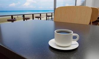 café negro en una taza blanca sobre una mesa de mármol. la cafetería o el restaurante tiene un balcón con vistas a la playa. vistas al mar y la playa mar azul y cielo despejado. representación 3d foto