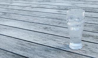 agua clara o soda en un vaso transparente para cerveza. agua fría en un vaso con cubitos de hielo, burbujas en el vaso. colocado en un piso de tablones hay una luz que brilla en el vidrio. representación 3d foto