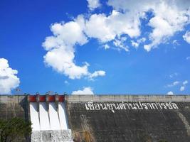 el texto blanco significa khun dan prakan chon dam. presa de riego está liberando agua. cielo azul brillante y nubes blancas. atracciones principales de la provincia de nakhon nayok, tailandia foto