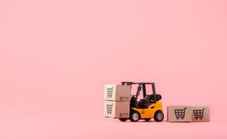 Logistics, and delivery service - Forklift model and paper cartons or parcel with a shopping cart logo on Pink background. Shopping service on The online web and offers home delivery. photo