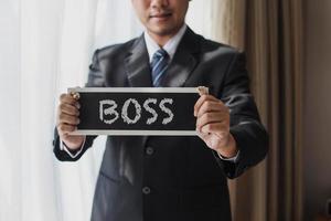 Cropped shot of Businessman in black suit and tie with Boss sign board photo