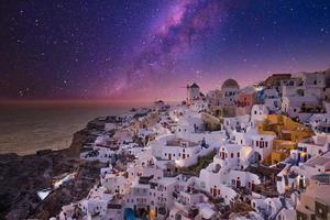 Oia village in sunset light with stars and milky way, Santorini, Greece. Amazing summer vacation landscape, white architecture and evening lights. Famous travel destination, urban travel background photo