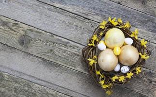 Wooden texture with golden and yellow eggs in a nest with flowers. Copy space for your easter text photo