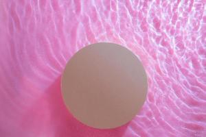 Top view of empty round podium in transparent waves of water on pink background. Blank cosmetic product photo