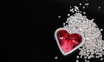 A red diamond or a large ruby in the shape of a heart, a symbol of love or Valentine's Day. A red diamond is placed on a pile of small diamonds. On the black reflection. 3D Rendering. photo