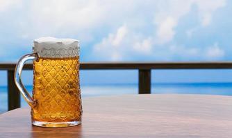 cerveza artesanal o de barril en un vaso transparente alto con espuma de cerveza encima y burbujas en el vaso. cerveza fría en un vaso, colocada sobre una mesa de madera en la playa, el mar durante el día. representación 3d foto