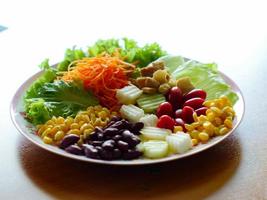 Fruit salads have yellow corn in the foreground and have other parts blur in the background like tomatoes and carrots. photo