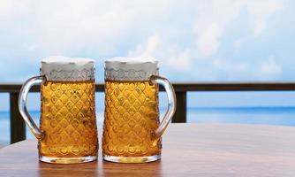 Draft or craft beer in a tall clear glass With beer foam on top And there are bubbles in the glass. Cold beer in a glass, placed on a wooden table on the beach, the sea during the day. 3D Rendering photo