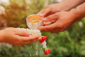 Young man's hands pour water and flowers on elder hand holding jasmine garland for Songkran festival photo