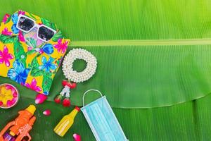 fondo del festival songkran con flores de guirnalda de jazmín en un tazón de agua, perfume y piedra caliza sobre un fondo verde de hoja de plátano húmedo. foto