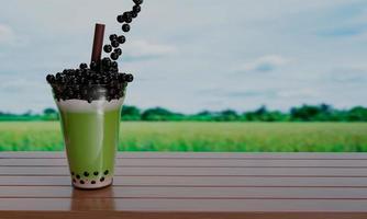 té verde con leche de burbujas en un vaso transparente y pajitas marrones colocadas sobre una mesa de madera y desdibujan el fondo del campo de arroz. representación 3d foto