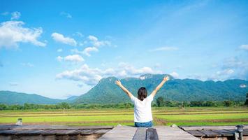 The girl held up two hands and breathed fresh. show independent symptoms Sit by a wooden bridge on a rice field, nature, clear air. Grasslands, mountains, and clear skies. photo