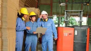 equipe de trabalhadores de fábrica da indústria em uniforme de segurança e capacete inspeciona o armazenamento por laptop, pedido de estoque no armazém, pilhas de gerenciamento de empilhamento de papelão com empilhadeira, logística de fabricação de produtos. video