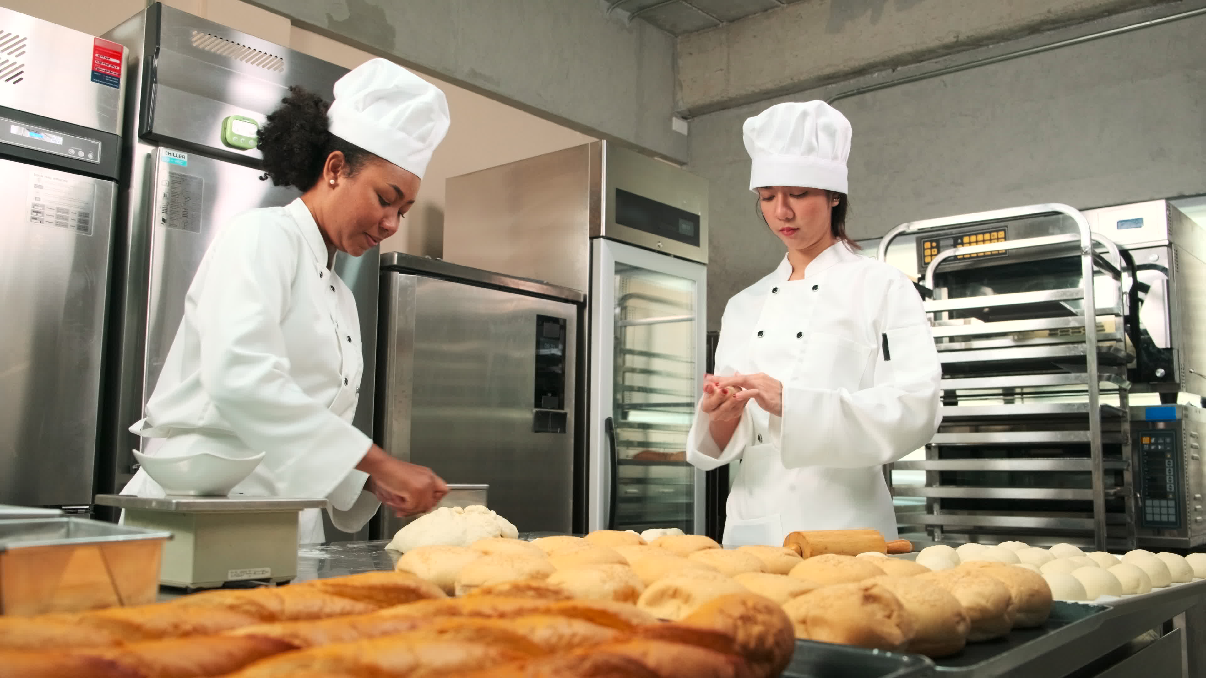 Two professional female chefs in white cook uniforms and aprons knead