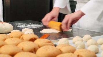 Close up of chefs' hand in white aprons and cook uniforms are kneading raw pastry dough, preparing bread, cakes, cookies, and fresh bakery food, baking in oven, stainless steel kitchen of restaurant. video