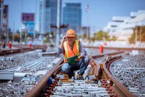 ingeniero ferroviario bajo control del proceso de construcción prueba de trenes y control del trabajo ferroviario en la estación de ferrocarril con comunicación por radio. ingeniero con uniforme de seguridad y casco de seguridad en el trabajo. foto