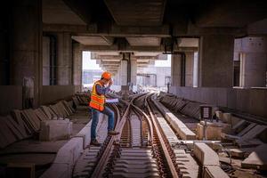 ingeniero ferroviario bajo control del proceso de construcción prueba de trenes y control del trabajo ferroviario en la estación de ferrocarril con comunicación por radio. ingeniero con uniforme de seguridad y casco de seguridad en el trabajo. foto