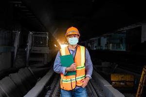 ingeniero ferroviario bajo control del proceso de construcción prueba de trenes y control del trabajo ferroviario en la estación de ferrocarril con comunicación por radio. ingeniero con uniforme de seguridad y casco de seguridad en el trabajo. foto