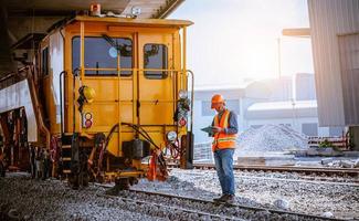 ingeniero ferroviario bajo control del proceso de construcción prueba de trenes y control del trabajo ferroviario en la estación de ferrocarril con comunicación por radio. ingeniero con uniforme de seguridad y casco de seguridad en el trabajo. foto