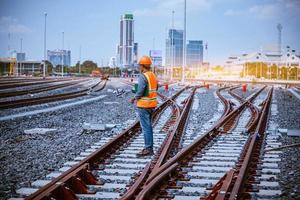 ingeniero ferroviario bajo control del proceso de construcción prueba de trenes y control del trabajo ferroviario en la estación de ferrocarril con comunicación por radio. ingeniero con uniforme de seguridad y casco de seguridad en el trabajo. foto