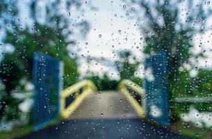 Rain droplets on the surface of car glass with blurred green nature and bridge background through window glass of car covered by raindrops. Freshness after rain. Wet windscreen shot from inside car. photo