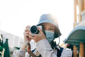Young adult asian woman backpack traveller wear face mask take a photo by camera.