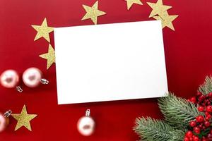 maqueta navideña, estrellas brillantes y adornos con tarjeta en blanco para copiar espacio sobre fondo rojo. foto