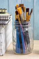 Artist workspace, assorted of brush in glass jar on wooden tabletop with sketchbooks. photo