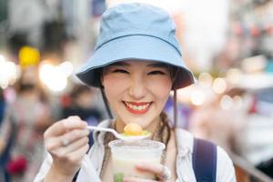 Closeup young adult asian foodie woman backpack traveller eating asia dessert street food. photo