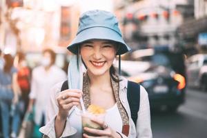 joven adulta asiática foodie mujer mochila viajero comiendo postre asiático en la comida callejera de Chinatown. foto