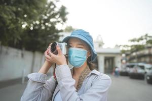 Young adult asian woman backpack traveller wear face mask take a photo by camera.