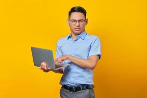 un joven asiático pensativo asiático con gafas usando un portátil aislado de fondo amarillo. concepto de empresario y emprendedor foto
