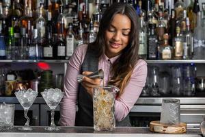 Positive female barkeeper making cocktail in bar photo