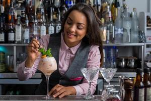 Happy Hispanic woman decorating cocktail in bar